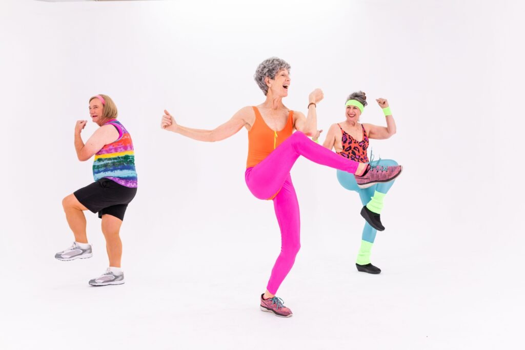 Three senior women having fun and staying fit with energetic aerobics in colorful outfits indoors.